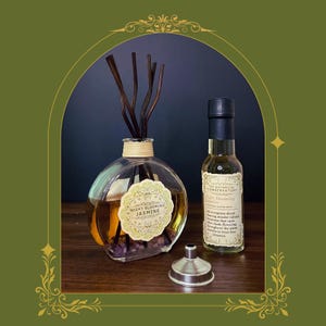 May include: A round glass reed diffuser with dark sticks, filled with amber liquid and purple stones, featuring a label reading Night Blooming Jasmine. Beside it is a tall bottle labeled The Botanical Conservatory and a small metal funnel.