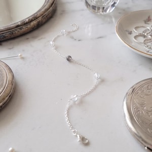 Peut inclure: Un bracelet délicat en chaîne argentée orné d'une série de petites perles transparentes et translucides, entrecoupées d'une perle gris foncé unique. Le bracelet est composé de fins maillons métalliques et d'un fermoir mousqueton sécurisé.