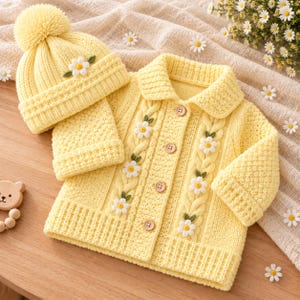 Può includere: Un set in maglia giallo pallido composto da un cardigan e un berretto abbinato. Il cardigan presenta un colletto, cinque bottoni in legno, pannelli a treccia e applicazioni di margherite bianche. Il berretto include un grande pon-pon.