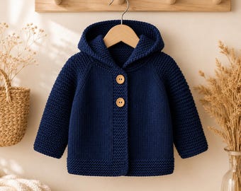 May include: A dark navy blue hooded cardigan made of a thick, textured knit fabric. The garment features long sleeves, a hood, and two large, round, light-colored wooden buttons centered on the front placket. The knit pattern is consistent throughout.