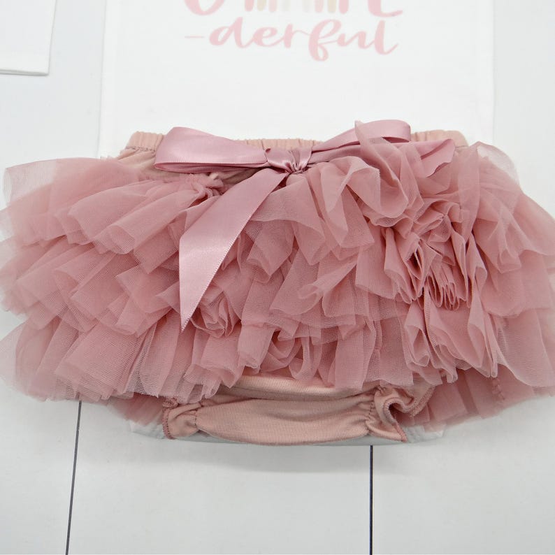 May include: A dusty rose tulle baby bloomers with a satin bow. The bloomers have multiple layers of tulle and are perfect for a special occasion.