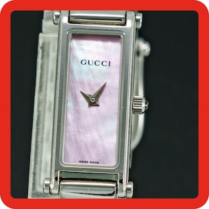 May include: A rectangular Gucci wristwatch featuring a silver-tone metal case and a light pink mother-of-pearl dial. The watch face displays the Gucci logo at the top and the text Swiss Made at the bottom, with two silver-tone hands.