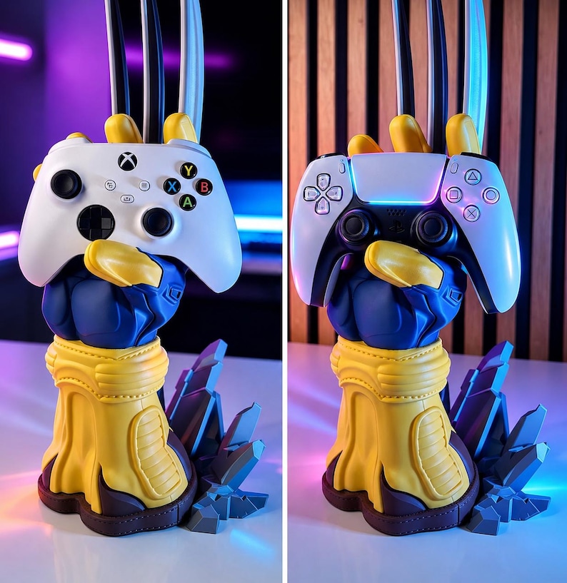 May include: A blue and yellow gloved hand sculpture with three metallic claws extending upward, designed as a controller stand. The base features jagged gray rock-like elements. The stand is shown holding a white Xbox controller and a white PlayStation controller.
