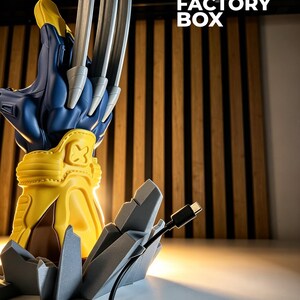 May include: A blue and yellow glove-shaped lamp with three long silver claws extending from the top. The base is a gray jagged rock formation. A black USB-C charging cable is attached to the side. The text 3D FACTORY BOX is visible.