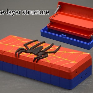 May include: A rectangular three-layer storage box featuring a red lid with a yellow spiderweb pattern and a black spider emblem. The base is blue. A second open box shows the internal tiered structure with the text Bambu Lab embossed inside.