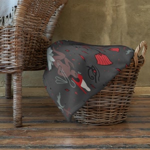 Könnte beinhalten: Eine dunkelgraue Tagesdecke mit einem sich wiederholenden Muster aus roten Blumen, stilisierten Figuren und geometrischen Formen. Die Decke liegt über einem Weidenkorb.