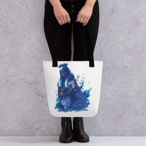 Könnte beinhalten: Eine weiße Einkaufstasche mit einer blauen Illustration einer Person mit einer Krone und Blumen. Die Person ist von blauen Blumen und wasserartigen Spritzern umgeben.