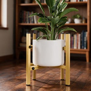 May include: A white cylindrical ceramic planter pot held within a gold-colored metal stand. The stand features four vertical legs with black caps at the top and bottom, connected by a cross-brace structure with black adjustment knobs.