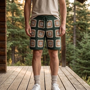 May include: Crochet shorts featuring a dark green base with a repeating granny square pattern in shades of white, tan, and dark green. The shorts include a drawstring waistband and are worn with a plain beige t-shirt, light socks, and white sneakers.