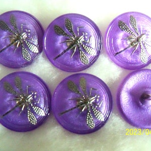 Peut inclure: Six boutons violets avec des motifs de libellules argentées. Les boutons sont ronds et ont une finition brillante.