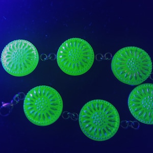 May include: A green glass necklace with a chain and round pendants. Each pendant features a floral design.