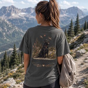 May include: A charcoal gray short-sleeve t-shirt featuring a graphic print on the back of a black Labrador retriever sitting in a forest landscape with flowers, birds, and the text Mountain Grace Co. Outdoors with small heart icons.