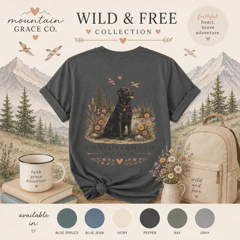 May include: A charcoal gray t-shirt featuring a graphic of a black Labrador retriever sitting in a forest with flowers. The text reads Mountain Grace Co. Outdoors, Wild & Free, and faithful heart, brave adventure. Includes a mug and backpack.