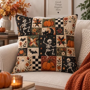 May include: A square throw pillow featuring a patchwork design with Halloween-themed illustrations including skeletons, pumpkins, ghosts, black cats, bats, and stars in a color palette of orange, black, cream, and green with a quilted texture.