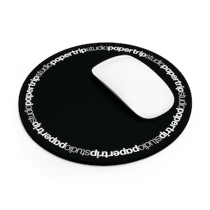 May include: A round black mouse pad featuring the white text papertripstudio repeated in a circular pattern along the outer edge. A smooth white computer mouse is positioned on the right side of the black surface of the circular mouse pad.
