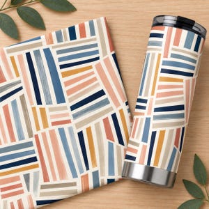 May include: A cylindrical stainless steel tumbler and a matching square fabric item featuring a geometric pattern of vertical and horizontal stripes in shades of navy blue, light blue, muted orange, soft pink, and beige on a cream background.