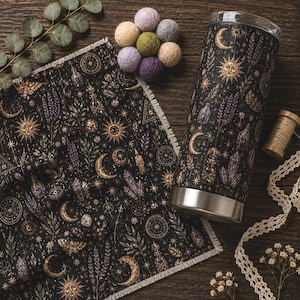 Può includere: Un panno in tessuto nero con bordi sfrangiati e un bicchiere in acciaio inossidabile abbinato, entrambi caratterizzati da una stampa celeste di soli dorati, lune, stelle, lavanda viola, cristalli e falene, accompagnati da piccole sfere di lana.