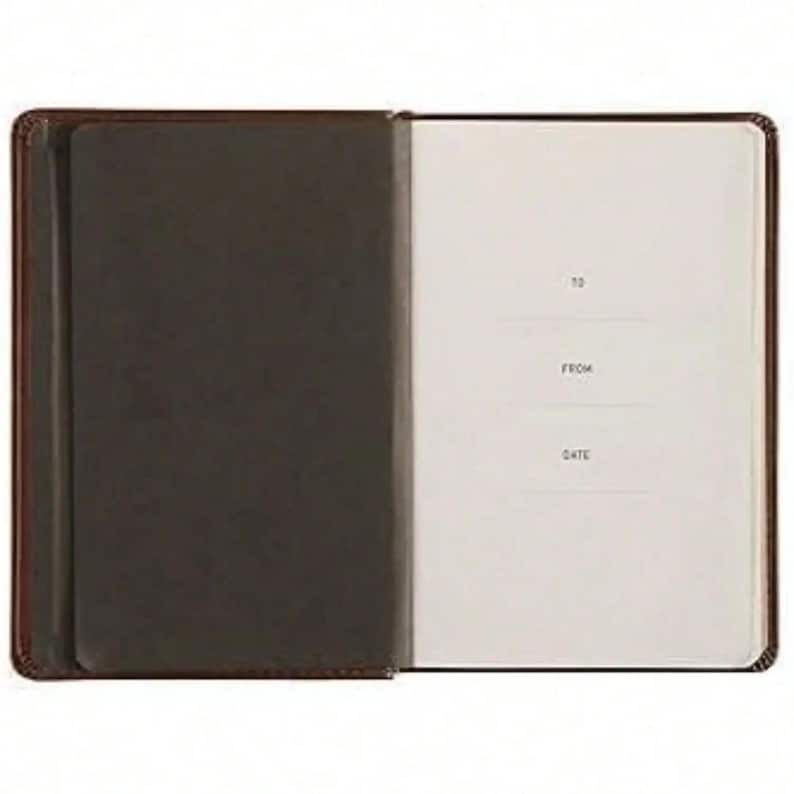 Puede incluir: Un cuaderno abierto con una cubierta de color marr&oacute;n oscuro y una solapa interior del mismo color en el lado izquierdo. La p&aacute;gina derecha es de color blanco roto y presenta el texto impreso TO, FROM y DATE, con l&iacute;neas para escribir.