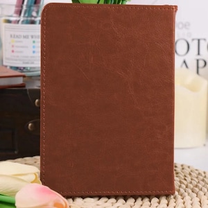 Puede incluir: Un cuaderno rectangular con una cubierta de color marr&oacute;n texturizado que presenta costuras visibles a lo largo de los bordes. La superficie tiene un aspecto ligeramente desgastado con pliegues sutiles y un acabado mate uniforme.