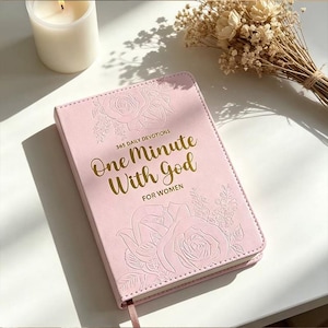 May include: A light pink devotional book titled One Minute With God For Women, featuring gold foil lettering and embossed floral patterns on the cover. The book includes 365 daily devotions and has a thin ribbon bookmark attached at the bottom.