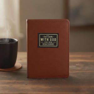 Puede incluir: Un libro encuadernado en cuero marr&oacute;n con una etiqueta negra rectangular en la portada. La etiqueta presenta el texto blanco One Minute WITH GOD FOR MEN. El libro tiene un acabado liso y mate y est&aacute; colocado en posici&oacute;n vertical sobre madera.