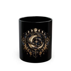 May include: A black ceramic mug featuring a detailed gold and white illustration of a coiled snake wrapped around a crescent moon. The design is surrounded by a circular arrangement of moon phases, stars, and ornate filigree accents.