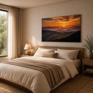 K&ouml;nnte beinhalten: Ein rechteckiger Wandkunstdruck, der einen leuchtenden Sonnenuntergang &uuml;ber geschichteten Gebirgsz&uuml;gen in Orange-, Gold- und tiefen Violettt&ouml;nen zeigt, platziert &uuml;ber einem Bett mit neutraler Bettw&auml;sche und einer Nachttischlampe.