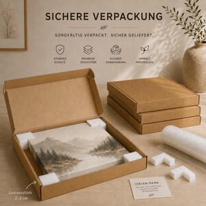 May include: A brown cardboard shipping box containing a landscape canvas print of mountains and trees. The box includes white foam corner protectors. Text on the box includes 'SICHERE VERPACKUNG' and 'VIELEN DANK'. A note indicates a 2-3 cm depth.