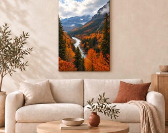 May include: A vertical rectangular wall art print depicting a mountain landscape during autumn. The scene features a winding river flowing through a valley filled with vibrant orange and yellow trees, framed by tall evergreen pines and distant peaks.