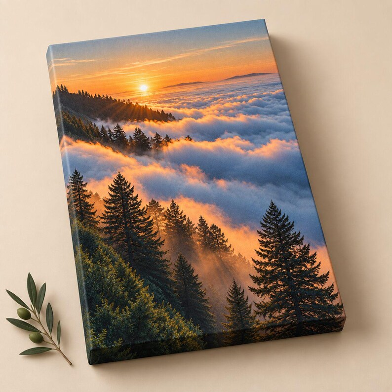 May include: A rectangular canvas print featuring a landscape of dark green pine trees on a mountainside overlooking a thick layer of clouds at sunset. The sun glows orange and yellow above the horizon, casting light across the misty sky.