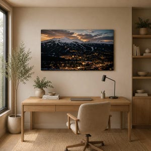 May include: A rectangular wall art print featuring a panoramic landscape of a snow-capped mountain range at dusk, with a glowing town nestled at the base. The scene displays dark blue and orange sky tones above the illuminated mountain slopes.