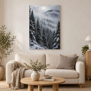 May include: A vertical wall art print depicting a dense forest of snow-covered evergreen trees on a mountainside. The scene is shrouded in thick, low-hanging fog and mist, creating a monochromatic palette of deep grays, whites, and blacks.