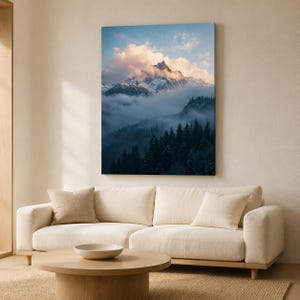 Könnte beinhalten: Ein vertikaler, rechteckiger Wandkunstdruck, der einen schneebedeckten Berggipfel zeigt, der teilweise von weichen rosa und weißen Wolken verdeckt wird. Unter dem Berg liegt ein dichter Wald aus dunkelgrünen Kiefern in einem dichten, blauen Nebel.