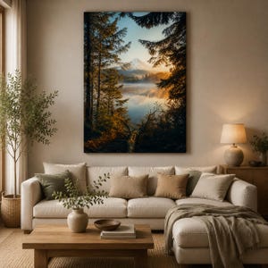 May include: A rectangular wall art print depicting a serene mountain landscape at sunrise, framed by dark silhouetted pine trees overlooking a calm, reflective lake with a soft mist, displayed above a beige sectional sofa in a living room.