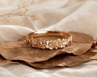 Könnte beinhalten: Ein Ring aus Roségold mit einem detaillierten botanischen Band aus geformten Blättern und kleinen Blüten. Mehrere winzige, klare, rund geschliffene Steine sind in der Mitte der floralen Motive gefasst und verleihen der Oberfläche Glanz.
