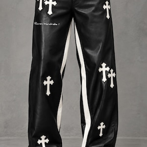 May include: Black faux leather pants featuring white cross-shaped patches distributed across the front. The pants include white side stripes running down the legs and the text Raven Wardrobe I printed in white on the upper right thigh area.
