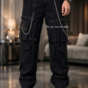 Könnte beinhalten: Schwarze Cargohose mit mehreren Utility-Taschen, verstellbaren Riemen mit Kunststoffschnallen und silberfarbenen Metallketten an D-Ringen. Der Text Raven Wardrobe ist in Weiß auf dem oberen Oberschenkelbereich aufgedruckt.