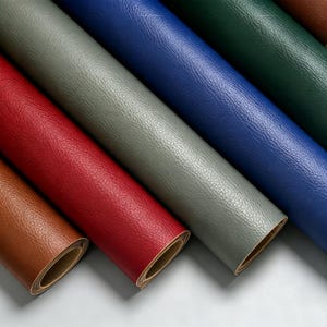 May include: Multiple rolls of textured faux leather material arranged diagonally. The colors include brown, bright red, light gray, royal blue, dark green, and a hint of dark brown. Each roll shows a consistent pebbled surface texture and a tan backing.