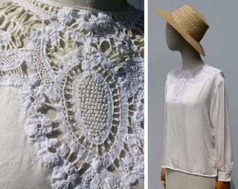 May include: White blouse with a delicate lace collar. The lace is a detailed pattern of circles and flowers.