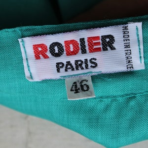 May include: A close-up of a teal fabric with a white label. The label reads "RODIER PARIS" in red and black text, with "46" below. The label also says "MADE IN FRANCE".