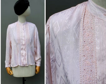 May include: A pink silk blouse with a geometric pattern and embroidered trim. The blouse has a mandarin collar and long sleeves.