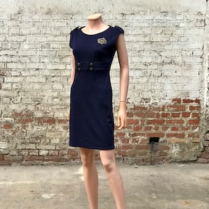 May include: A navy blue dress with short sleeves and a gold button detail at the waist. The dress has a fitted silhouette and a slightly flared skirt.
