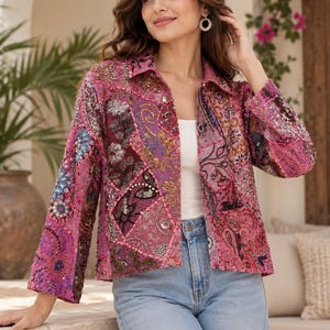 Op de afbeelding: Een jas met lange mouwen en een levendig roze patchworkontwerp met ingewikkeld kralenwerk, lovertjes en geborduurde bloemen- en paisley-patronen. De jas heeft een klassieke kraag, een knoopsluiting aan de voorzijde en wordt gedragen over een wit topje en een blauwe spijkerbroek.