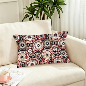 May include: A rectangular throw pillow featuring a repeating pattern of concentric circles in shades of black, white, cream, and deep red. The design consists of small dots arranged in circular bands, creating a dense, textured visual effect.