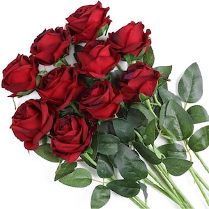 Könnte beinhalten: Ein Strauß aus dunkelroten künstlichen Rosen mit mehrschichtigen Blütenblättern und realistischen grünen Blättern an langen Stielen. Das Arrangement besteht aus mehreren zusammengefassten, blühenden Blütenköpfen in einer satten, karmesinroten Farbpalette.