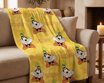 May include: A yellow fleece throw blanket featuring a repeating pattern of the cartoon character Goofy wearing a green hat and orange sweater, interspersed with the word Goofy printed in a light yellow font across the fabric surface.