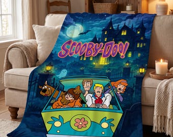 May include: A soft fleece throw blanket featuring a vibrant Scooby-Doo graphic. The design displays the Mystery Machine van with Scooby-Doo, Shaggy, Velma, Fred, and Daphne in front of a spooky haunted mansion under a full moon and night sky.