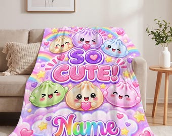 May include: A soft throw blanket featuring a colourful pattern of smiling, cartoon-style dumplings in shades of purple, blue, green, and beige. The text reads SO CUTE! and Name, surrounded by rainbows, yellow stars, and pink hearts.