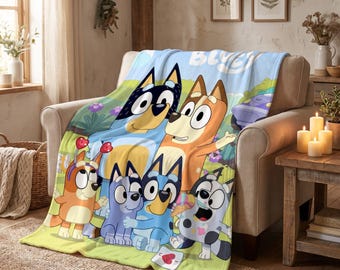 May include: A soft fleece throw blanket featuring a colourful graphic print of the Bluey characters including Bluey, Bingo, and their parents. The design shows the animated dog family in a grassy outdoor setting with the word Bluey at the top.