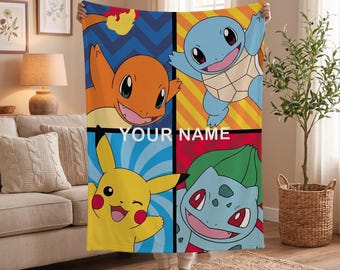 May include: A rectangular fleece blanket featuring a four-panel grid design with illustrations of Pikachu, Charmander, Squirtle, and Bulbasaur. The centre of the blanket displays the white text YOUR NAME against a dark horizontal divider line.